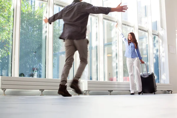 Woman with luggage waving to boyfriend at airport