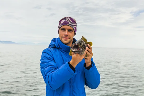 Young man with sea bass. Fishing off the coast of Kamchatka.