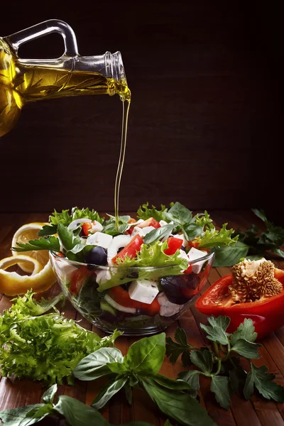 Greek salad with olive oil pouring from a bottle.