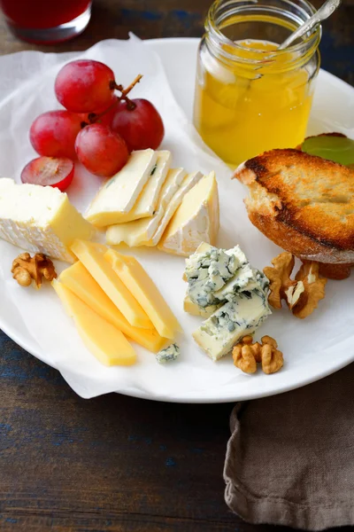 Cheese plate with grapes, honey, bread and walnuts on wooden background