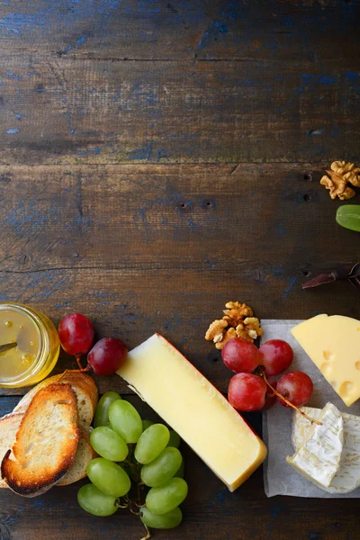 Three types of cheese with grapes, honey, bread and walnuts. Empty space background