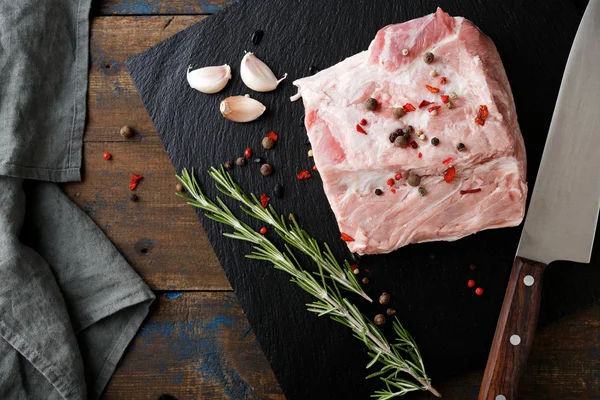 Piece Steak of Raw Pork Meat, a knife and ingredients for cooking on black slate
