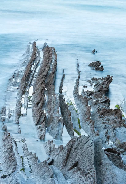 Twilight ocean coast with ribbed stratiform rock.