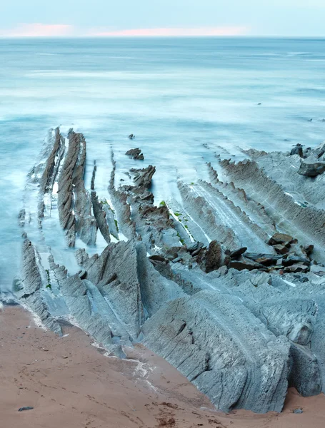 Twilight ocean coast with ribbed stratiform rock.