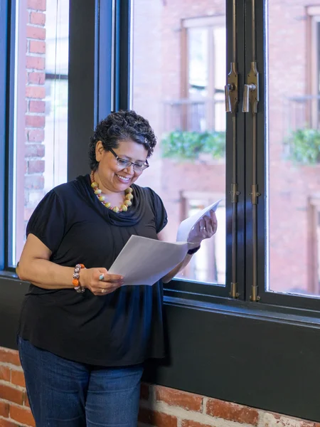 Hispanic Female Standing By Window Holding Papers In Office Setting