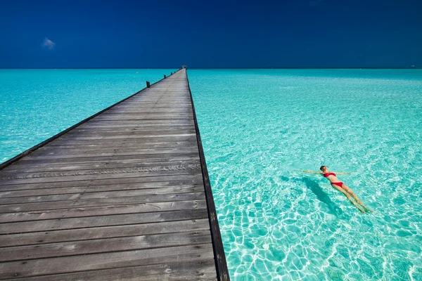 Young woman in red bikini swimming next to jetty in azure water