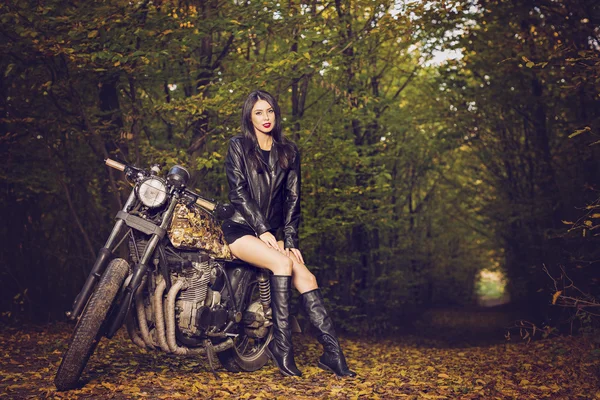 Biker girl in a leather jacket on a motorcycle posing in nature