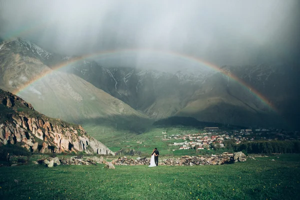 Unique wedding photo of the pair on a rainbow background and rain in the mountains