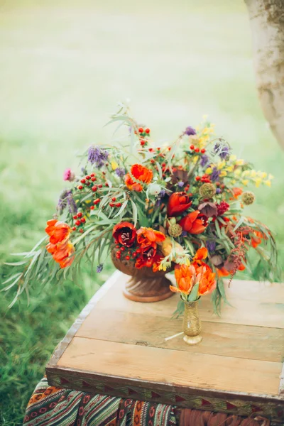 Beautiful wild red flowers are metal in a bronze vase on the chest outdoors on a grass background