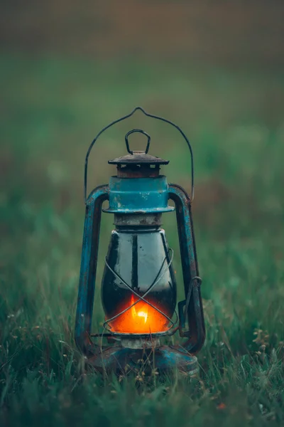 Burning vintage kerosene lamp stands on green grass at sunset