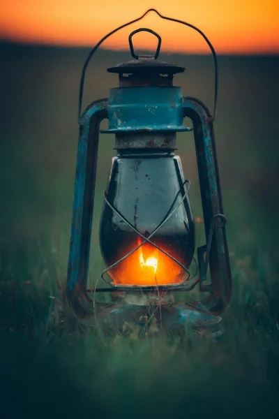 Blue burning vintage kerosene lamp stands on green grass at sunset