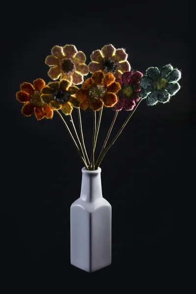 Bouquet of felted wool in a white vase on a black background, backlit