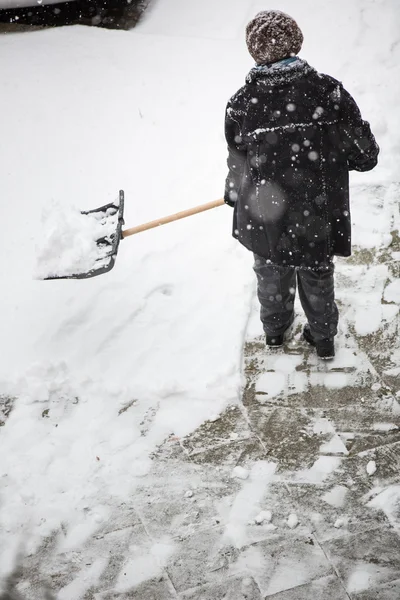 Woman shoveling snow from the sidewalk in front of his house after