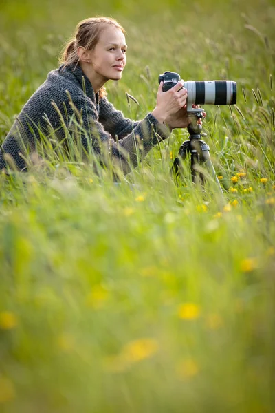 Pretty young woman with a DSLR camera outdoors, using a tripod,