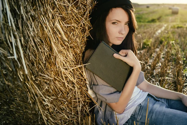 Girll hipster reads book against hay bale in fall