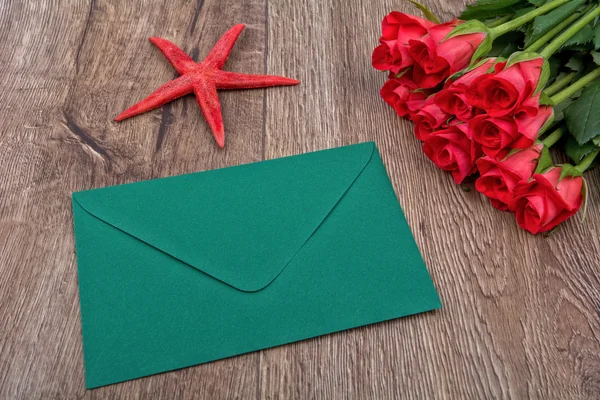 Green envelope, red roses and starfish on a wooden background
