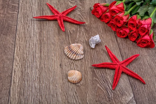 Starfishes, shells and red roses on a wooden background