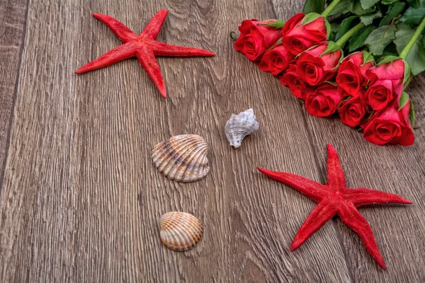Starfishes, shells and red roses on a wooden background