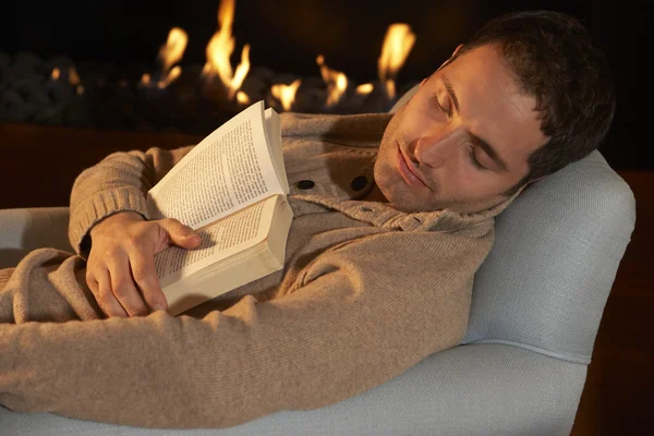 Man asleep with book in front of fire