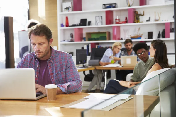 Businessman Working On Laptop In Busy Office