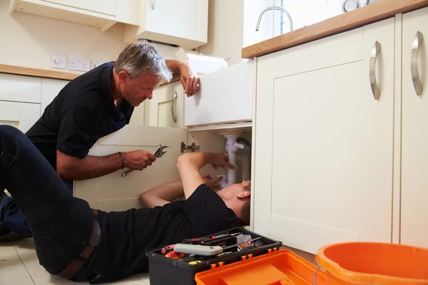Plumber teaching an apprentice to fix a kitchen sink