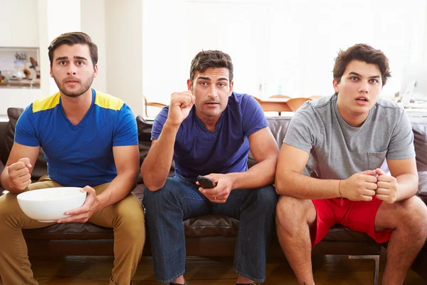 Group Of Men Sitting On Sofa Watching Sport Together