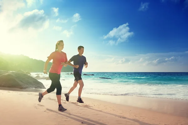 Man and woman running on tropical beach at sunset
