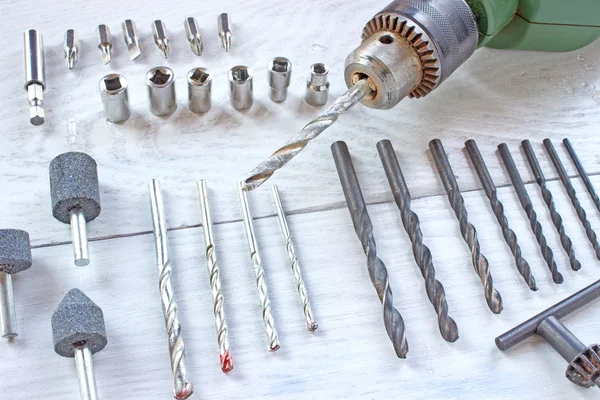 Electric drill and set of drill bits on wooden background