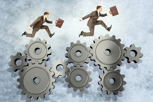 Two businessmen running on wheel gears