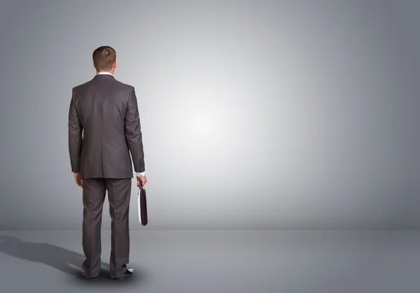 Businessman standing in an empty gray room. Rear view