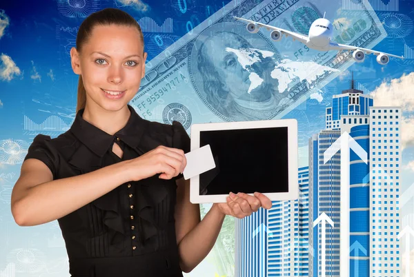 Beautiful businesswoman holding tablet and white empty card near screen. Buildings with money as backdrop