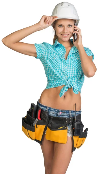 Woman in hard hat and tool belt calling on mobile phone