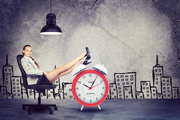 Businesswoman sitting with her feet up on alarm-clock