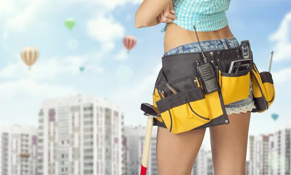 Woman in tool belt standing backwards. Cropped image. High-rise buildings as backdrop