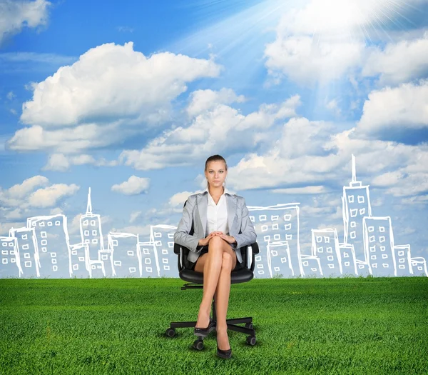 Woman in jacket sits on chair. Background of sketch building, grass