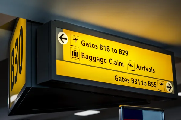 Yellow airport signage suspended by the ceiling in a terminal, telling passengers important information about their gates, where baggage claim, departures and arrivals are, etc