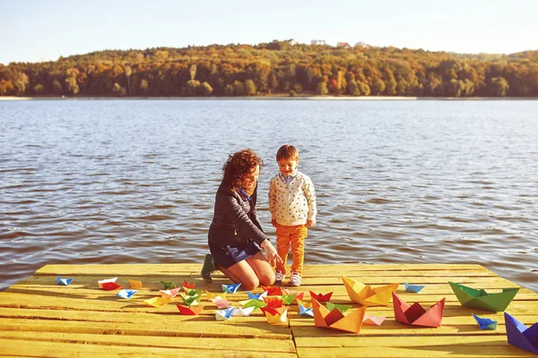 Mom and son playing with paper boats by the lake