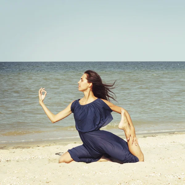 Young beautiful woman doing yoga at seaside in blue dress