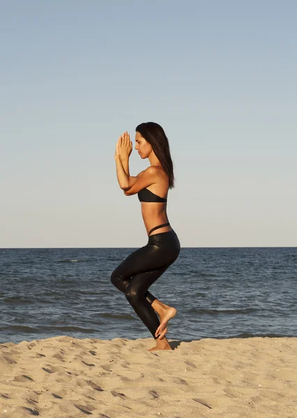 Young beautiful woman doing yoga on beach in black sport costume
