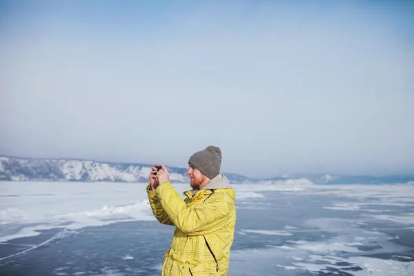 Bearded man in a bright jacket photographed standing on the ice of the frozen lake