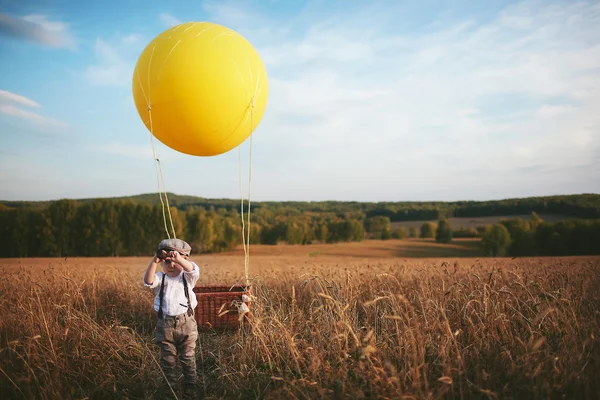 Little traveler boy looks through a telescope next to the balloon in a field