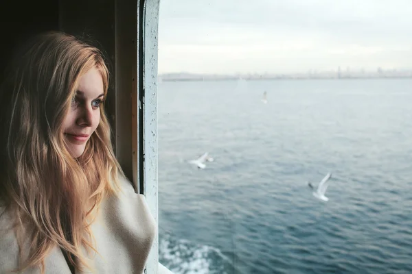 Blonde girl at a window overlooking the sea