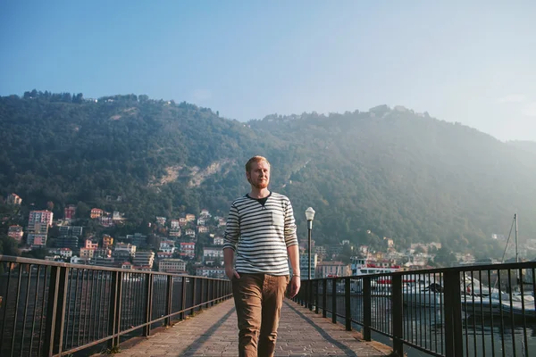Bearded man standing on the pier of a mountain lake Como