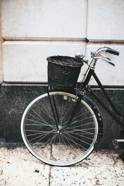 Black bicycle with a basket by the wall