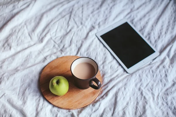 Tablet and an apple and tea lying on the bed