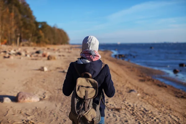 Girl with a backpack standing with her back to the shore