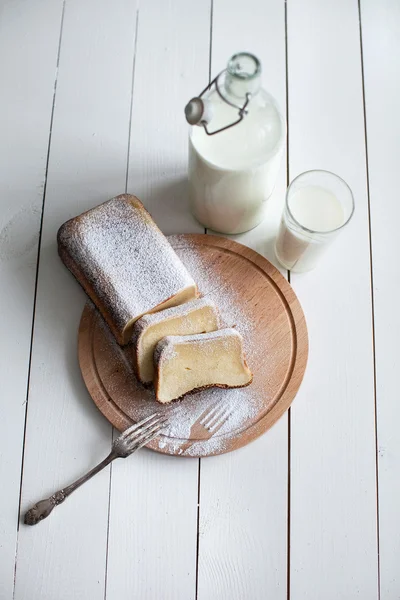 Chopped cake on a wooden base with a fork and milk
