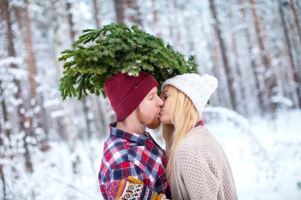 Young couple kissing with fir twigs walk in the winter woods