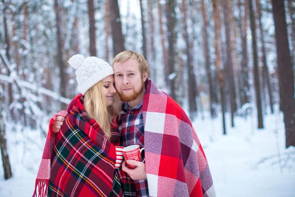 Young couple sheltered plaid holding a hot tea in winter wood