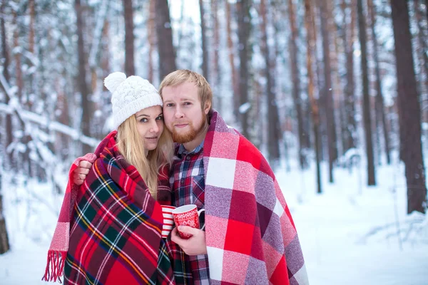 Young couple sheltered plaid holding a hot tea in winter wood